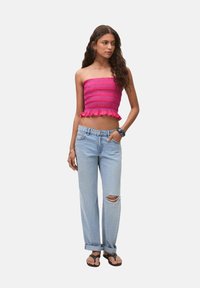 Lyserød smocket bandeau-top med flæsekant, parret med lyseblå slidte denimjeans, der har opfoldede manchetter, og sandaler.