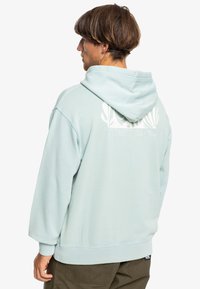 Light blue hoodie with a large white graphic design and logo on the back. Made of soft material, featuring a spacious hood and ribbed cuffs.