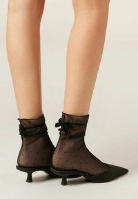 Sorte spidse sko med en kitten hæl, suppleret med gennemsigtige sorte ankelstrømper med prikker og samlede lace detaljer.