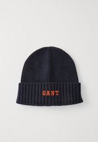 Gorro de punto azul marino con textura acanalada, que presenta un puño doblado y un logotipo bordado de "GANT" en naranja en la parte frontal.