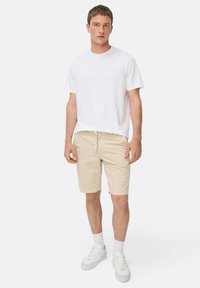 Weißes kurzärmliges T-Shirt, beige Shorts mit Kordelzug, weiße Sneaker und weiße Socken. Einfaches Design, weicher Stoff und bequeme Passform.