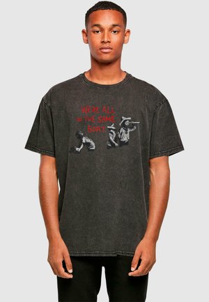 Musthave suur must puuvillane T-särk, millel on graafika kolme figuuriga ja punane tekst "OLEME KÕIK SAMAS PAATIS." Kulunud tekstuur.