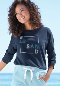Marinefarbendes Langarmshirt mit einem Grafikdesign in kontrastierenden Farben, kombiniert mit hellblauen Jogginghosen mit Kordelzug. Glatte Stoffqualität, lässige Passform.