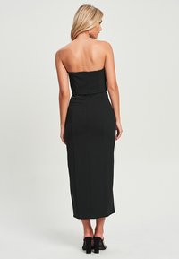 Schwarzes, trägerloses Midikleid mit einem taillierten Oberteil, einer glatten Textur, vertikalen Nähten und einem verdeckten Rückenreißverschluss, kombiniert mit hohen Sandalen.