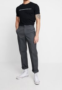 Černé bavlněné tričko s potištěným textem, šedé kalhoty rovného střihu a bílé vysoké tenisky. Neformální outfit s ohrnutými rukávy.