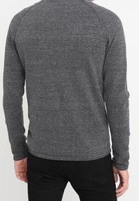 Ciemnoszara koszula z długim rękawem z teksturowanej tkaniny, z okrągłym dekoltem i rękawami typu raglan, zestawiona z czarnymi spodniami.