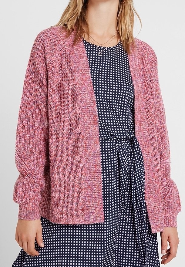 Cardigan rosa a trama con una vestibilità ampia, apertura frontale e maniche lunghe, abbinato a un vestito blu navy a pois. Materiale in maglia morbida.
