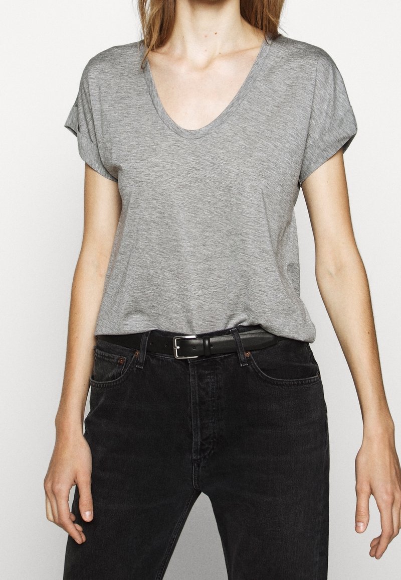 Graues Baumwoll-T-Shirt mit V-Ausschnitt und aufgerollten kurzen Ärmeln, kombiniert mit schwarzen Jeans und einem schwarzen Gürtel. Schlichter, lässiger Stil.