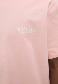 Šviesiai rožinė medvilninė marškinėliai su balta "SPIAGGIA Originals Studio" logotipu ant krūtinės. Minkšta tekstūra, trumpomis rankovėmis ir apvaliu kaklu.