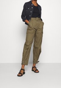 Dark denim jacket, black tank top, olive cargo pants with a belted waist, and buckle accents. Black sandals complete the outfit.