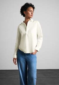 Lyse creme-farvet skjorte med krave, halvdels knaplukning, lange ærmer og en afslappet pasform, parret med højtbarmede blå denimjeans.