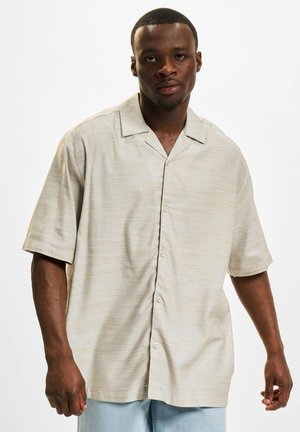 Kortermet, lys beige skjorte med teksturert mønster, knappefront og klassisk krage. Sammen med lyseblå jeans.