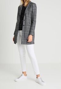 Gestreepte blazer in grijs met gestructureerd ontwerp en twee knopen, gecombineerd met een zwart met patroon top, witte slim fit broek en witte sneakers.