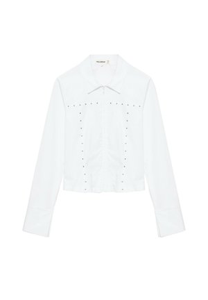 Weisse kurz geschnittene Jacke mit langen Ärmeln, Kragen, vorderem Reissverschluss und dekorativen kleinen Metallnieten, die das Vorderteil umrahmen.