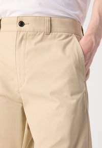 Beige bukser laget av glatt stoff, med knappelukking og sidelommer, med en skreddersydd passform og rene sømmer.