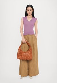 Brown woven leather handbag with a rounded shape, paired with a lavender sleeveless top and vertical striped wide-leg trousers.
