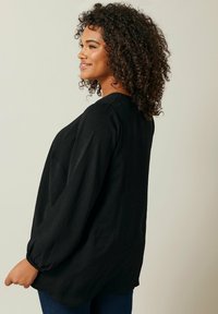 Schwarz, locker sitzende Bluse mit langen, leicht gepufften Ärmeln und Rundhalsausschnitt. Hergestellt aus leichtem Stoff, der eine dezente Textur aufweist.