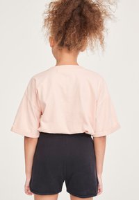 Rosa Baumwoll-T-Shirt mit überschnittenen Schultern, kombiniert mit schwarzen Shorts. Das T-Shirt hat aufgerollte Ärmel und einen lässigen Schnitt.