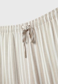 Tissu rayé vertical beige et blanc avec une ceinture élastique et un cordon noué au centre devant.