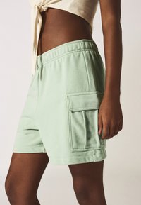 Pantaloni corti verde menta realizzati in tessuto misto cotone, caratterizzati da un ampio cintura elastica e una tasca applicata sul lato. Texture liscia.