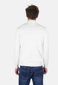 Maglione bianco lavorato a maglia con maniche lunghe, polsini e orlo a coste. Indossato con jeans in denim blu caratterizzati da un design classico con cinque tasche.