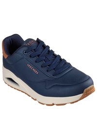 Baskets bleu marine avec partie supérieure perforée, accent de talon marron, semelle intermédiaire blanche épaisse et semelle extérieure en caoutchouc texturé. Les lacets sont de couleur bleu foncé.