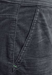 Tissu texturé gris montrant un gros plan d'une poche avec un détail de couture verte contrastante, mettant en valeur une apparence douce et tissée.