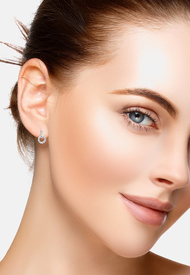 Söljör med cirkulär design, prydd med små klara ädelstenar. Nära bild av en models ansikte som visar detaljer kring örat och örhänget.
