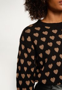 Maglione nero con scollatura rotonda, texture lavorata a maglia e motivi a cuore metallizzati oro su tutto il capo. Maniche lunghe e vestibilità comoda.