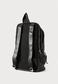 Black backpack with fabric and leather materials, rectangular shape, adjustable shoulder straps, front zipper pocket, and top handle.