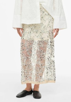 Gjennomsiktig beige skjørt med sølv paljetter, brukt med hvit brodert topp og svarte slip-on sko.