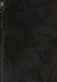 Schwarze Fleecejacke mit glatter, weicher Textur. Verfügt über einen Reißverschluss und ein geprägtetes Logo auf der Brust. Keine Muster oder zusätzlichen Details.