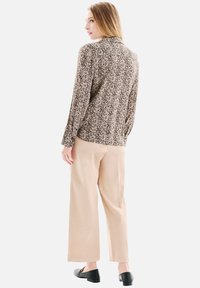 Chemise à manches longues à motif beige, fabriquée en tissu léger, associée à un pantalon large beige et des chaussures noires à enfiler.