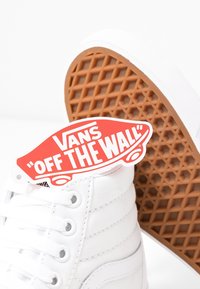 Baskets montantes blanches Vans avec semelle marron à motif gaufré et étiquette logo Vans "Off The Wall" rouge fixée aux lacets.