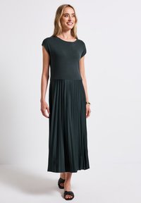 Robe maxi vert foncé avec un corsage ajusté et une jupe plissée. Fabriquée en tissu doux, avec des manches courtes et un col rond.