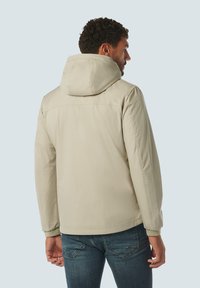 Lichtbeige hoodie-jack met een gladde afwerking, voorzien van een relaxte pasvorm en gestikte details, gecombineerd met blauwe jeans.