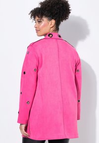 Růžová semišová bunda s rovnými liniemi, s černými akcenty a průchodkami na rukávech, hladká textura a límec na knoflíky.