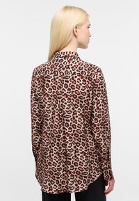 Lepelprint shirt met een tan basis en zwarte en rode vlekken, lange mouwen, een klassieke kraag en een licht afgeronde zoom.