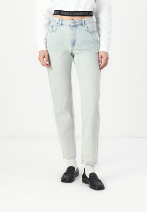 Jeans de tiro alto en azul claro con corte recto, que presentan bolsillos frontales y un acabado desgastado. Combinados con un suéter blanco y mocasines negros.