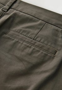 Pantaloni de culoare verde măsliniu, cu o textură netedă, având un singur buzunar posterior și detalii subtile de cusătură. Materialul pare durabil și bine structurat.