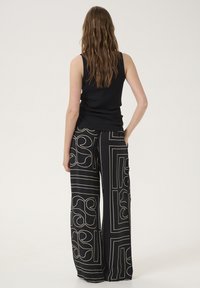 Black sleeveless top paired with wide-leg pants featuring white geometric patterns and textured fabric, shown from the back.