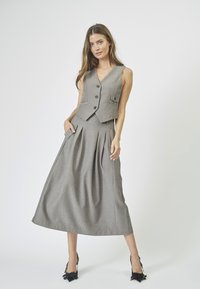 Gray tailored vest with a notch collar and front pocket, paired with a matching high-waisted, pleated maxi skirt. Black high-heeled shoes.