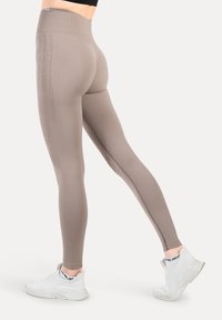 Leggings de talle alto en color topo, fabricados con material elástico y con detalles en las costuras laterales; combinados con zapatillas deportivas blancas.