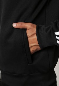 Black hoodie with a smooth texture, side pocket, and ribbed cuffs. Features three white stripes on the sleeve for detail.