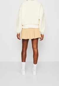 Nadměrná krémová chlupatá mikina s žebrovanými manžetami a lemem, doplněná plisovanou béžovou sukní a bílými teniskami s kotníkovými ponožkami.