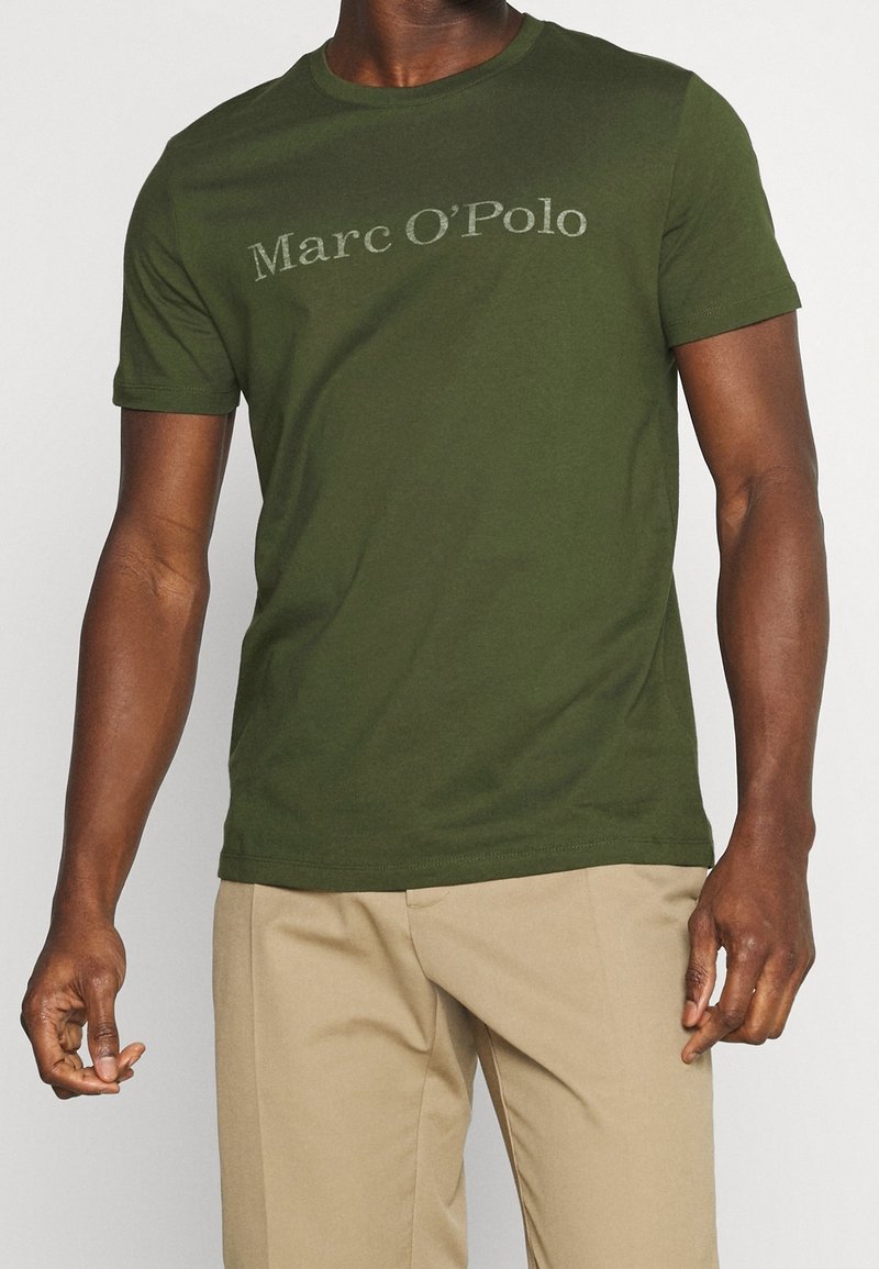 Mørkegrøn bomulds t-shirt med rund hals og mærkenavnet "Marc O'Polo" trykt i en lysere nuance hen over brystet.