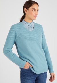 Maglione azzurro chiaro a scollo a V con motivo a maglia testurizzato sulle spalle e sulle maniche, dotato di polsini e orlo a costine, abbinato a una camicia a righe.