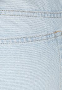 Vaaleansininen denim-kangas, jossa näkyy kudottu rakenne, ja jonka reunassa on sauma ja ompeluyksityiskohta.