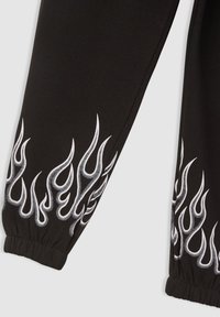 Czarne spodnie dresowe z białymi płomieniami na dolnej części nogawki, elastycznym mankietem i miękką fakturą tkaniny.