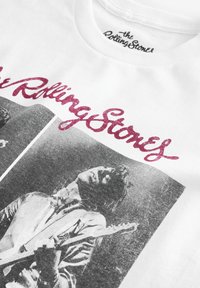 Hvid bomulds T-shirt med et stort gråt grafisk billede af en musiker og pink glitrende tekst "the Rolling Stones" ovenfor billedet.